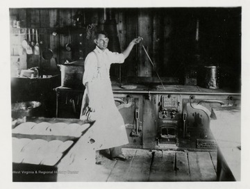 Man in front of an oven.  Note the loaves of bread, this lasts one day.  Note stove.  