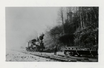 Train engine on tracks heading towards a cart.  Man standing on tracks.  