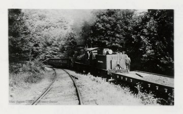 Train engine on tracks with engineer looking back out of the window. 