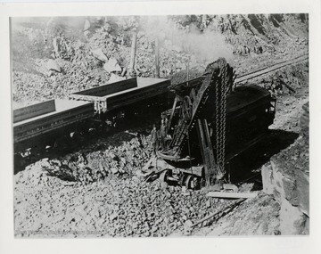 Men standing on big steam shovel beside dump cars.  