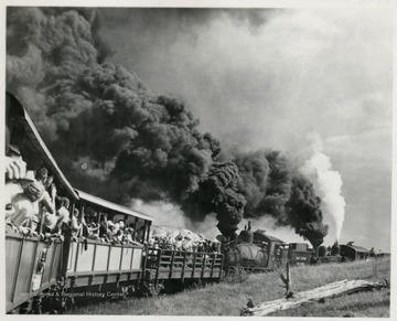 Two train engines pushing passenger cars up hill.