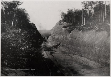 Distant photo of a Shay engine and steam shovel in between the cut in mountain.