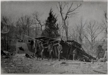 Men walking around the remains of a wrecked Shay train engine.