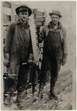 Two men pose next to a log cart.  