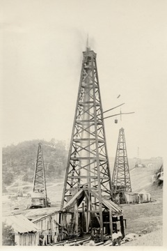 Five derricks and rigs.  Oil gushing from well in foreground.