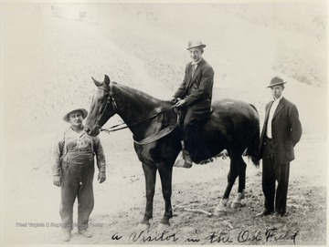 Man on a horse with two men standing beside the horse.  