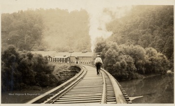 Man walking down tracks towards gas pumping station, Wetzel Co. 