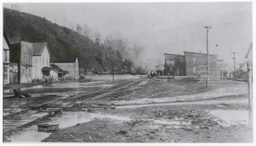 Town with a train track running in the middle of it.  Area has many mud puddles.