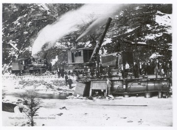 Shay locomotive and derrick car on tracks above derailed train engine.  Crew posing on engine.