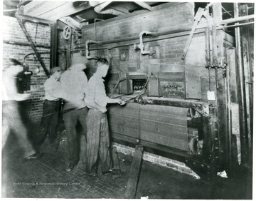 Men working at the Fostoria Glass Company.  Wine glasses visible inside machinery.