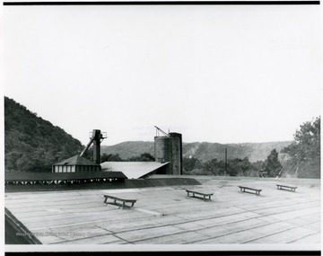 A roof top of a factory building with silos in the background.