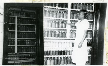 Bridget, an African-American Extension Service worker, displays shelves of canned Faraday food.