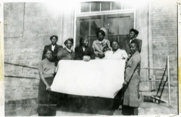 Group portrait of female African-American Extension workers holding a flag in front of a building. 