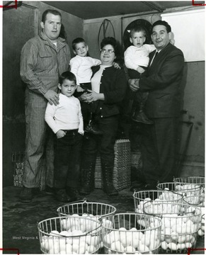 Group portrait of a family standing next to baskets of eggs. Left to right: Robert L. Kelly Robert William, 5 Richard 4, being held by Mrs. Kelly; and Charles 3, being held by State Director Manchin.