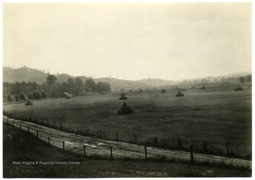 Stacks of hay in a broad valley with a house and barn in the distance. U.S. Dept. of Agriculture, Bureau of Agricultural Economics, Photographic Section, No. 18428.