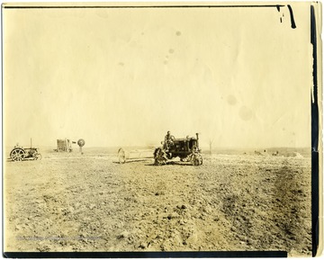 Men spreading lime with tractors on the fields at Arthurdale, getting ready for potatoes.  Small windmill visible in background.