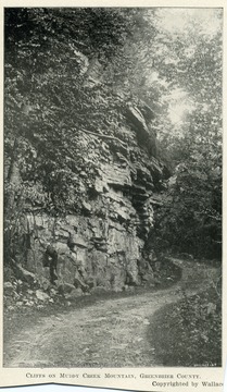 A winding mountain road towered over by rocky ridges. Copyrighted by Wallace.