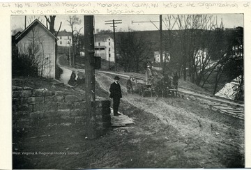 Picture of Cut No. 18 road in Morgantown, Monongalia County, W. Va. before the organization of W. Va. Good Roads Association. Picture has one man standing on the side walk and another man driving a horse drawn wagon in the street. From the Report of the W. Va. State Board of Agriculture for the Quarter Ending Sept. 30, 1908