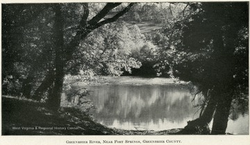 A river mirrors the distant bank full of leafy trees and a grassy hill. 