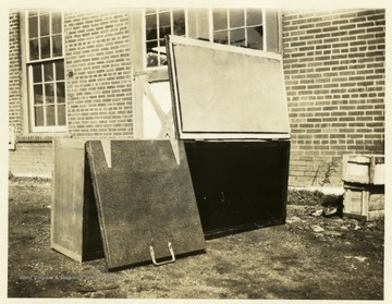 Front of a dynamite and cap box on its side with one lid open and one partially closed.