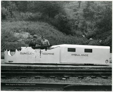 Two men of the Dunglen No. 11 Mine, owned by Hanna Coal Company, inspecting a piece of equipment in front of a ambulance coal cart.