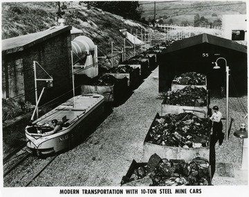 Miner in electric locomotive No. 15 hauling loaded coal cars on one track, while another miner inspects loaded coal carts on another track in a Consoldiation Coal Company, W. Va. mine yard.