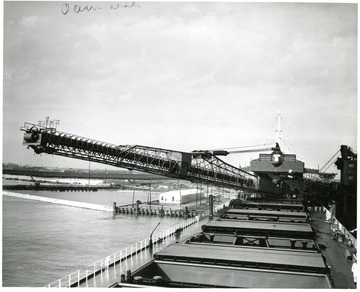 A ship has its boom extended into the harbor.  A train yard sits in the distance. Newport News Shipbuilding and Dry Dock Co. 