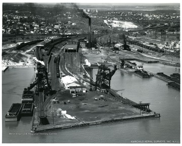 Text on back of photograph reads, 'Pictured is the new Pennsylvania Railroad pier at South Amboy, NJ. This pier is conveniently located to serve the entire New York Harbor territory, with facilities to accomodate a large number of boats. Two McMyler car dumpers, equipped with Seal-tite dedusters, with a combined capacity of 40,000 tons per 24-hour day are used.  Sufficient depth of water is maintained to accomodate vessels drawing not in excess of 20 feet of water.  Thawing plant facilities with an 86-car capacity are also provided for extremely cold weather.  Ample and conveniently located supporting track facilities are available to make possible rapid movement of loaded cars to the dumpers. Dimensions and gross weight of cars which can be handled over the No. 1 dumper are: Maximum length over couplers, 45 feet; maximum height, 11 feet, four inches; minimum height, six feet, six inches; maximum width, 10 feet, five inches; and maximum gross weight, 225,000 pounds.  Size of No. 2 machine is :  maximum length over couplers, 49 feet, maximum height, 12 feet; minimum height, six feet, six inches; maximum width, 10 feet, six inches; and maximum gross weight, 225,000 pounds.  The mailing address of this new pier is: Agent, Pennsylvania Railroad, South Amboy Coal Piers, South Amboy, N.J.  Telephone numbers are South Amboy 1-1959 and Pennsylvania 6-6000, extension 3015 and 3016.  F.E. Siepert, Extracted from Sawards's Journal, June 28, 1952 issue.'<br />