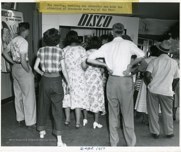 A crowd gathers around a Disco Fuel exhibit, to watch the snoring, mumbling man.  The Snoring, Mumbling Man Attracted and Held the Attention of Thousands Each Day of the Fair.