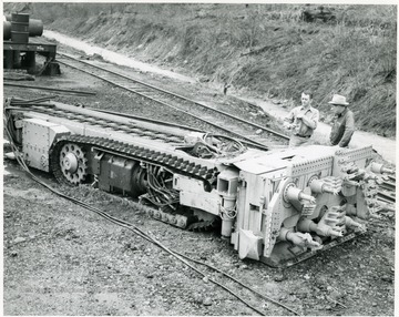 Two men standing next to a continuous mining machine.