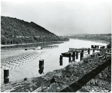 Coal barges being pushed on unknown river and unfilled barges just off shore.