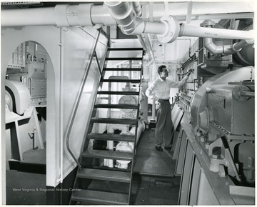 The engine room of the "Humphrey" towboat where an unidentified man inspects one of the main diesel propulsion engines.