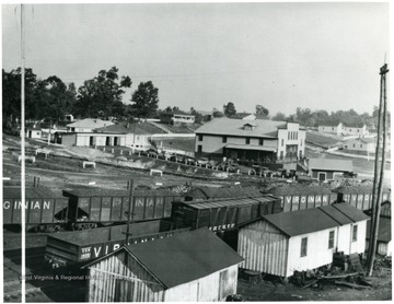 Coal cars beside some houses and the company store with cars in front of it. 