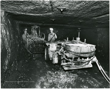 Two men with equipment putting up bolts to support the mine roof.