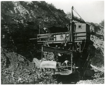 Caption on back reads, 'Stiff-arming a highwall is the job of this new, double-decker drill in operation at the Georgetown mine, Hanna Coal Co., at Georgetown, Ohio. Fruit of the ingenuity of coal mining engineers, the drill makes two blast holes at different levels in the highwall, permitting a blasting shot that brings down a large section of 'overburden.' The 'overburden,' rock, shale, limestone, clay and other mineral deposits, lies above the coal seam. Surface, or open-pit mining, accounts for 23 percent of total bituminous production. The Georgetown mine is the largest surface mine in the world.'