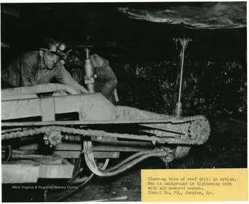 Close-up view of roof drill in action. Man in background is tightening bolt with air powered wrench at Consol. No. 204, Jenkins, Ky.