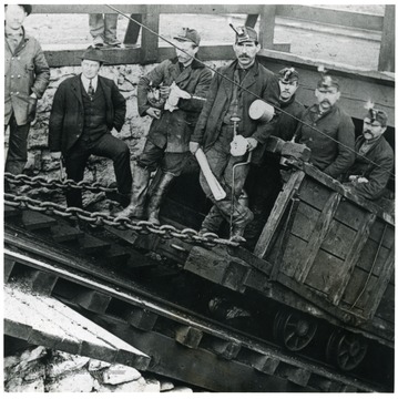 Men stand on a cart that is being pulled by a chain.