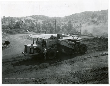 Man standing next to a scraper used for coarse mine waste disposal. Thickener and settling tank in the background.