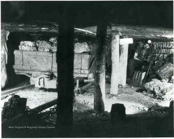 'This miner has just completed loading a mine car of weighing net about two and one-half tons, and is waiting for a locomotive to come along and take it out and give him another empty car. An industrious miner will load about six and sometimes eight of these cars in one day. This is a wooden mine car that is now being rapidly replaced by steel mine car equipment. The number of post shown in this picture indicate again the immense amount of timber required to conduct operations in a safe manner.'