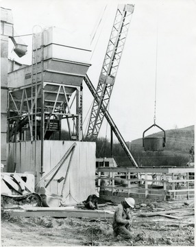 Two men working with cables while a crane is being used in the background.