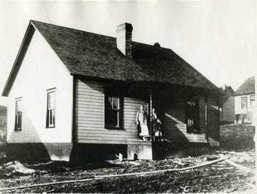 Women and child stand on porch of cottage.