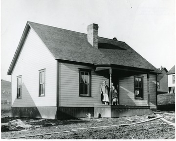 Women and child stand on porch of cottage.