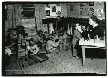 Woman inspects a child's mouth in a nursery while other children play.