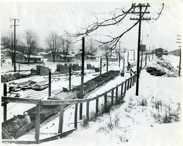 Men riding in coal cars along snow covered tracks to the Skelton mine during winter time.  Miner's homes and wood piles visible.