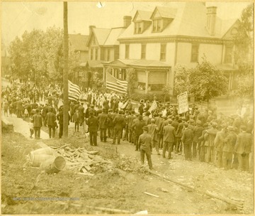 Miners fill the streets holding American flags and signs for eight hour work days and fair pay.