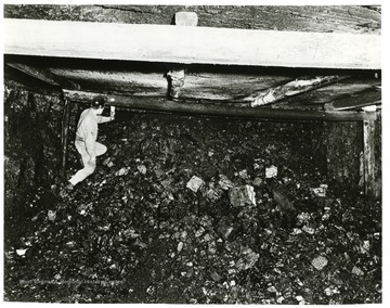 Miner stands on pile of coal ready to be loaded and sent out of mine.