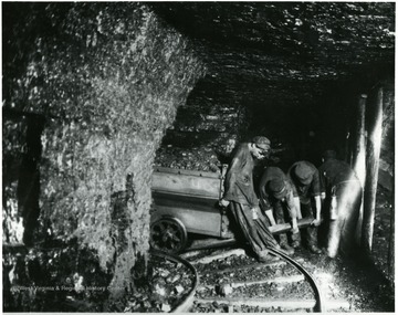 Group of miners attempt to realign the wheels of a coal car with the tracks in the mine. John Williams, Coal Life Project