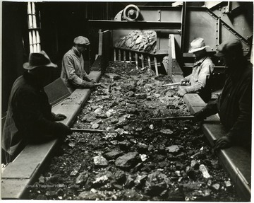 Miners examine coal on conveyor belt.