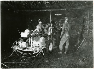 Two miners work on putting in roof bolts in the Pittsburgh Seam. Timber jack used to hold the roof while bolting.