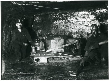 'All White Oak mines are electrically equipped and of course this mining machine is operated by electricity. The machine is mounted and transported on a specially designed truck and moves under its own power from one working place to another. It is taken from the truck by the machine operator and his helper and moved to the place of the coal and place in cutting position as you see it in this picture. The machine consists of an endless chain with 'bits' inserted, which act as cutters. The machine cuts a 'kerf' or hole along the bottom of the coal about 4 inches high and extending back six feet under the coal. The fine coal made by this machine is what is commonly known as 'bug dust.' Cutting machines are operated at night and each machine is capable of cutting twenty places on each shift. These machines are operated on tonnage basis and these operators earn high wages.'